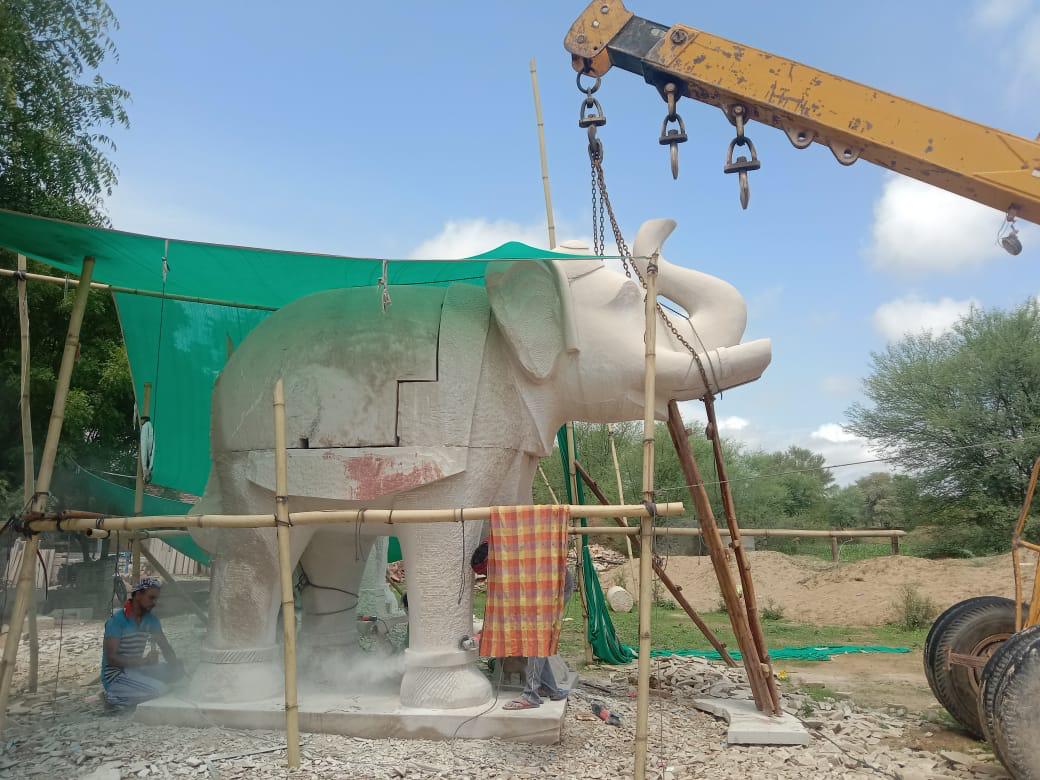 Stone elephant being carved under a shade net beside a crane – Kota Riverfront, Kota