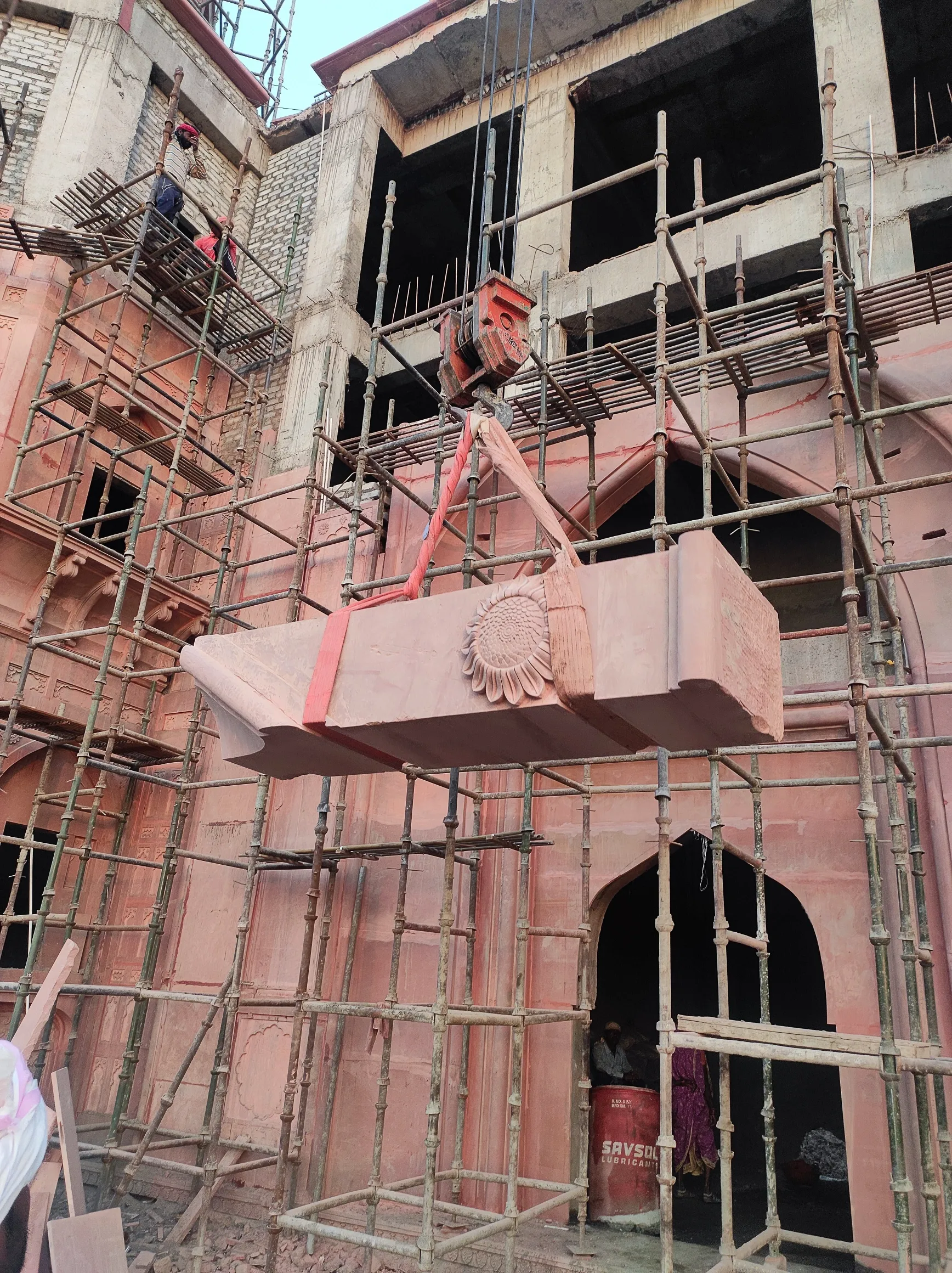 Crane lifting a sandstone facade block into a scaffolded elevation